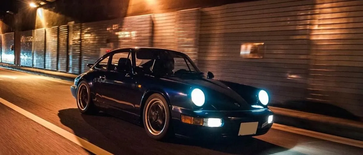 Auto negro clásico con faros encendidos en un túnel